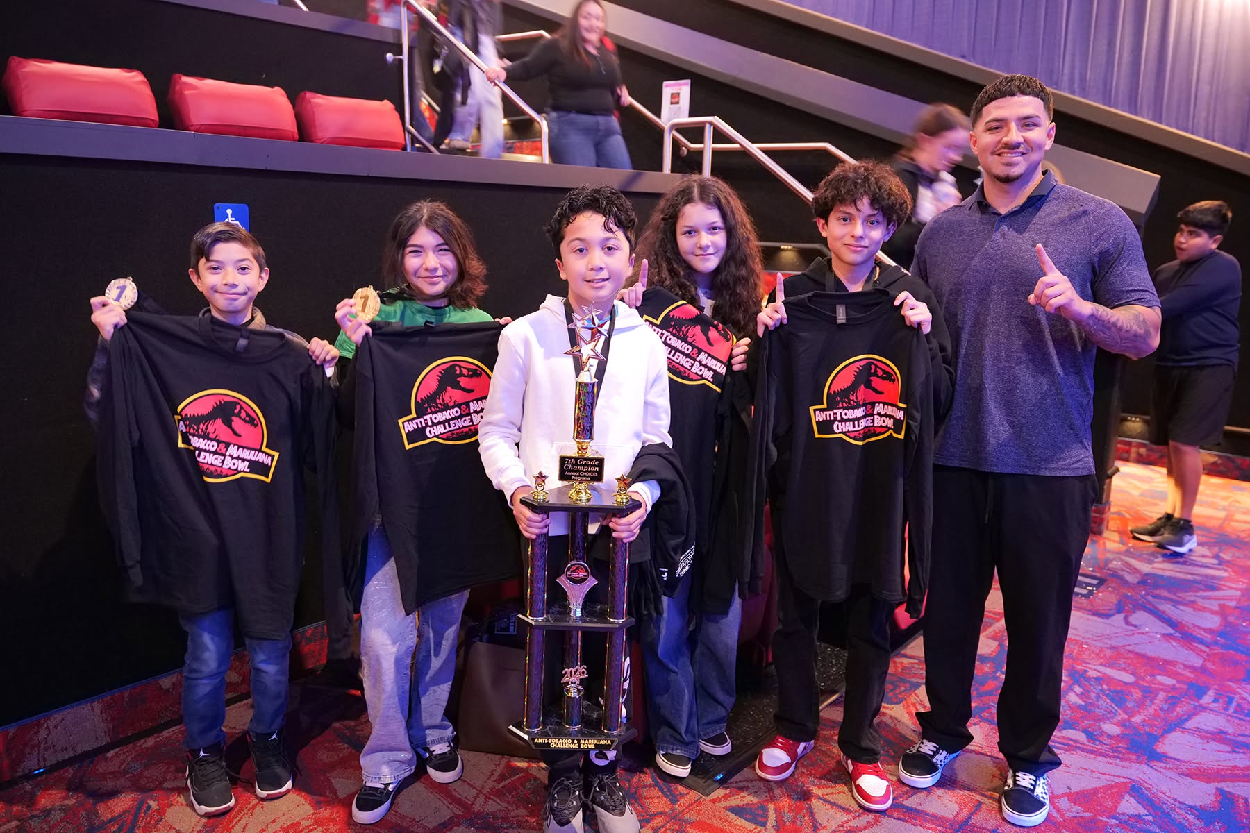 Students with first place trophy and event shirts in theatre.