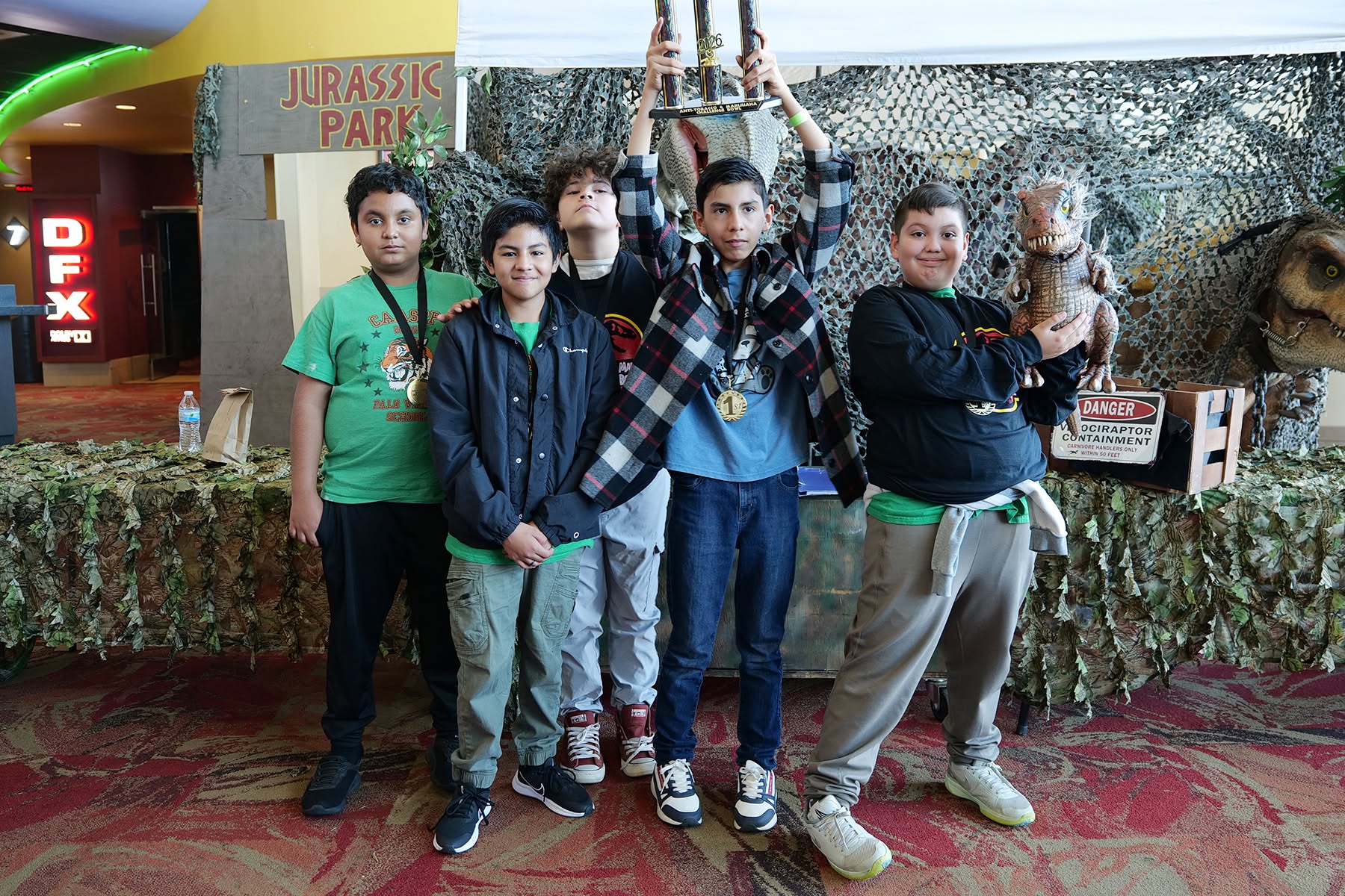 Students with a trophy in front of a dinosaur backdrop.
